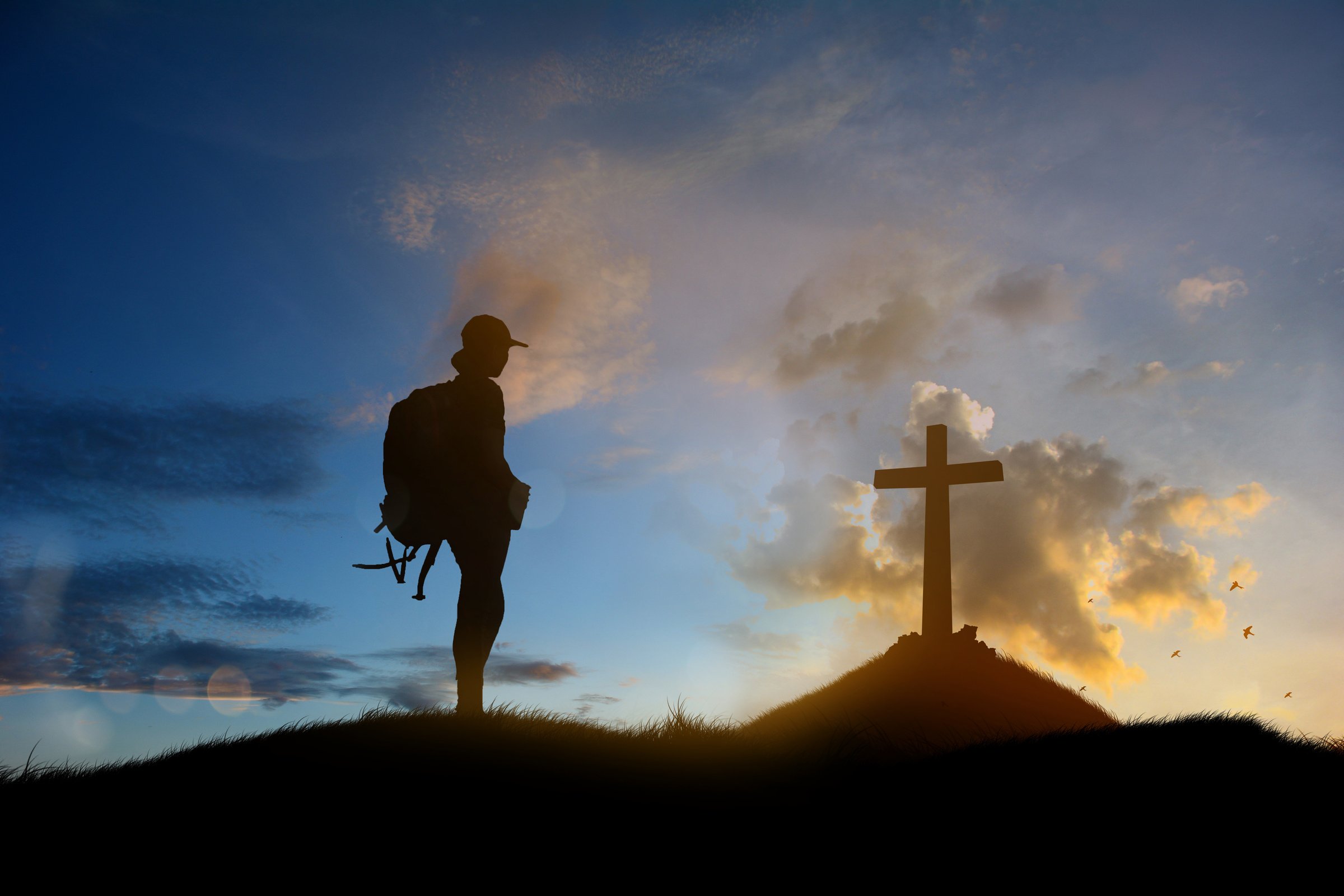 Man standing holding christian cross for worshipping God at sunset background.